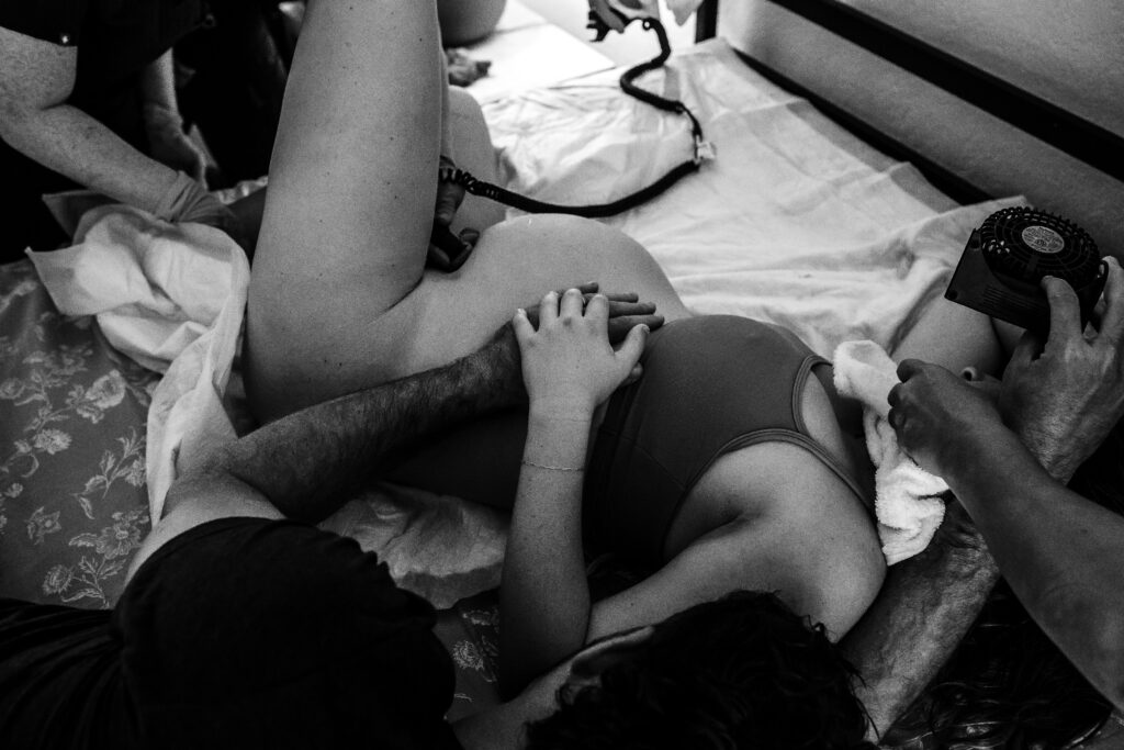 Black and white documentary home birth — baby crowning as family supports mother