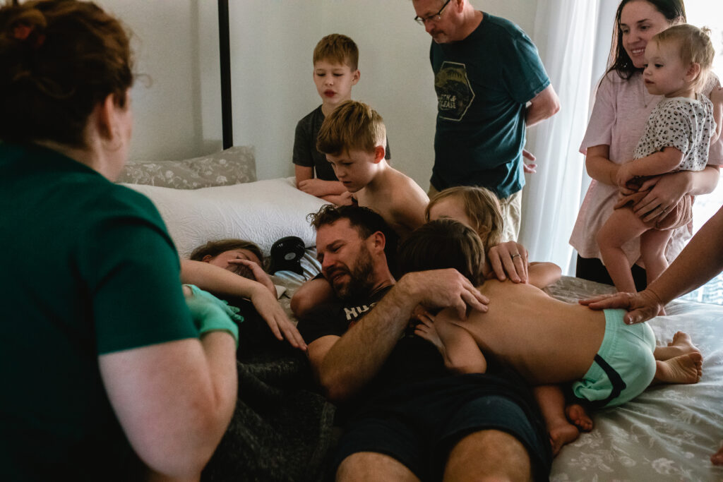 Big siblings leaning in close to meet their new baby for the very first time at home