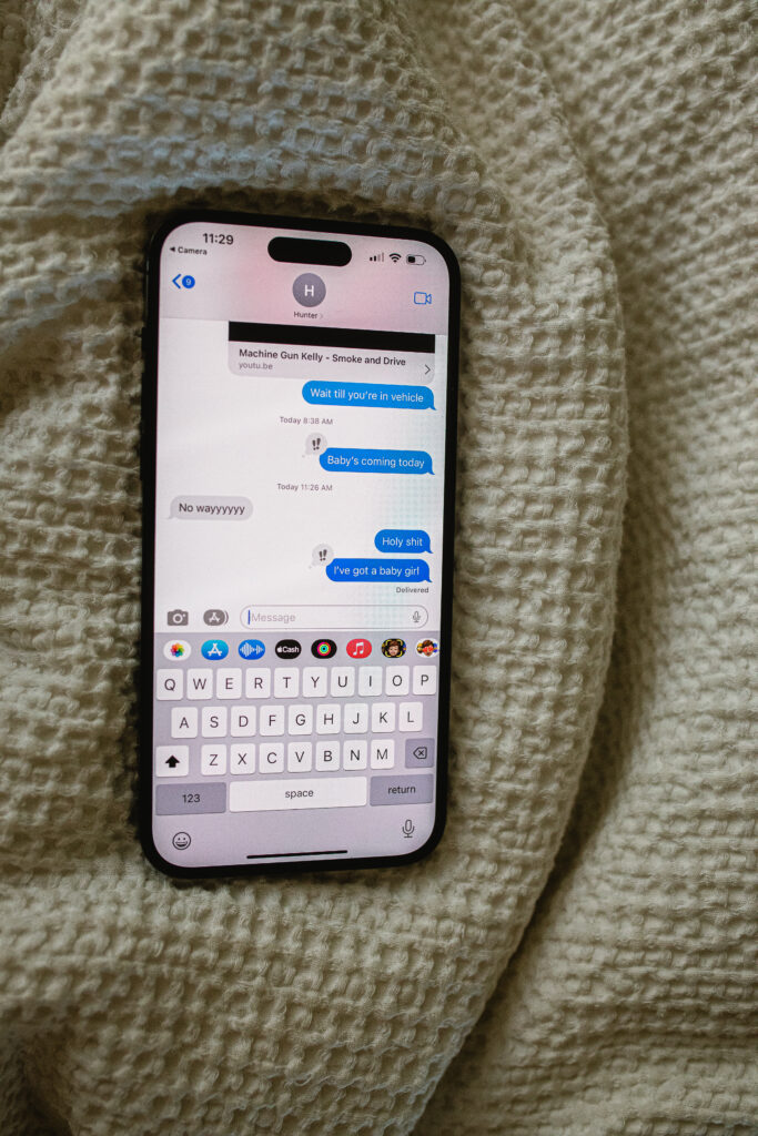 Documentary birth detail — iPhone on blanket showing first family birth announcement messages
