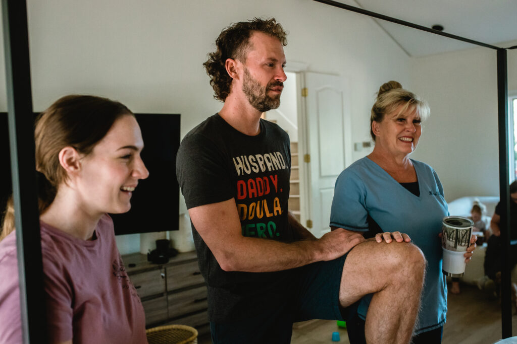 Father kneeling beside bed in quiet reflection during newborn bonding time after home birth