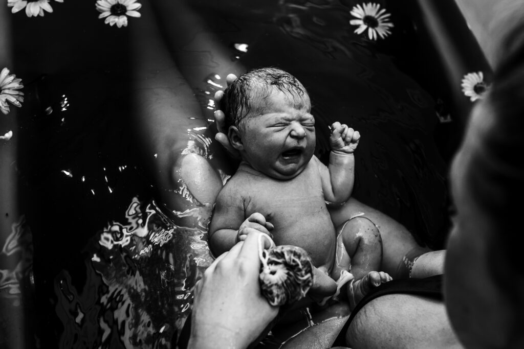 Close-up of newborn resting on father’s chest, tiny hand curled against his shirt