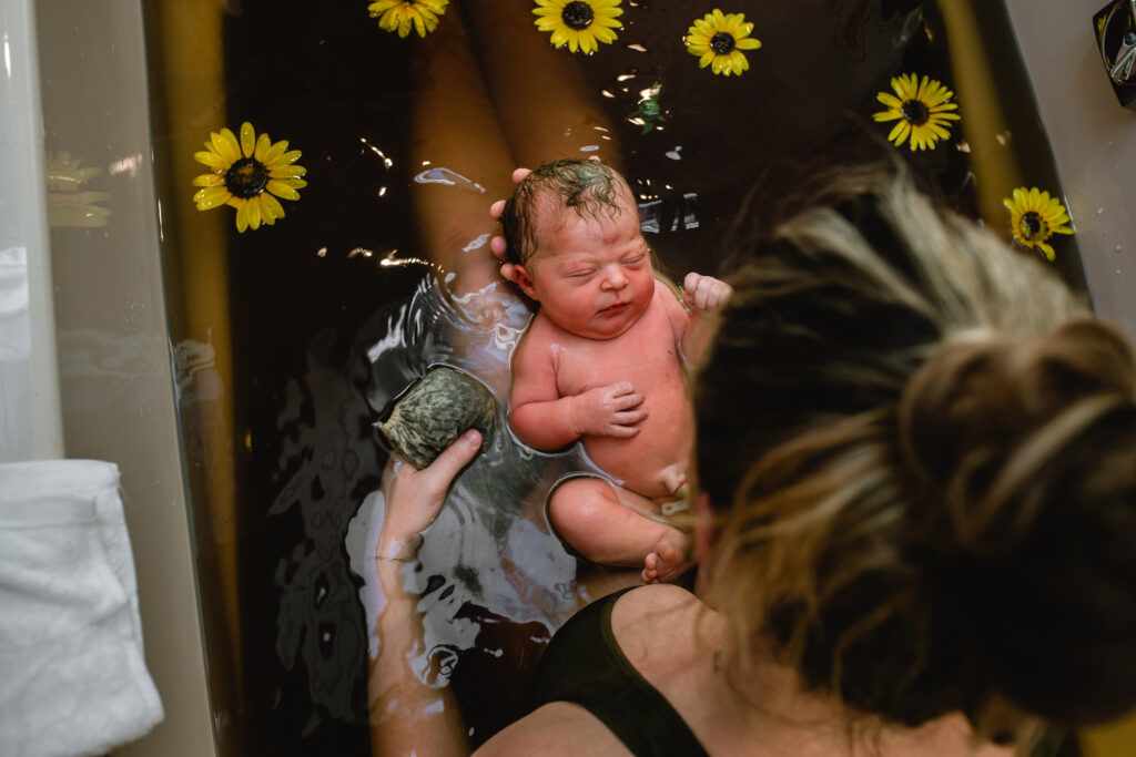 Father sitting in armchair holding newborn in soft natural window light after home birth