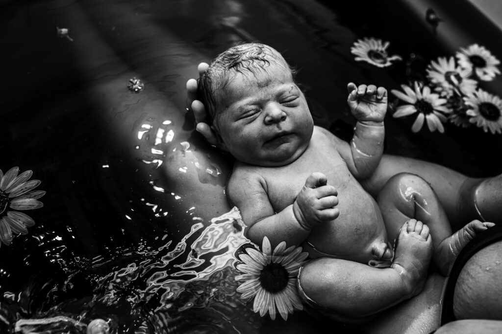 Newborn floating peacefully in herbal bath while mother supports baby in her arms