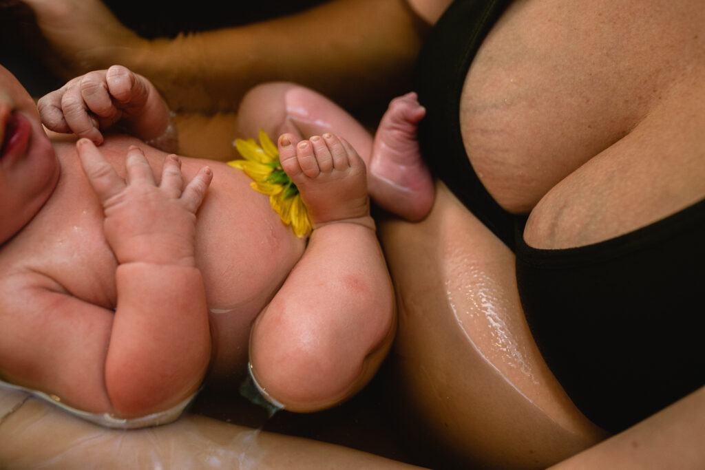 Close-up of newborn in herbal bath with eyes closed, water rippling gently around baby