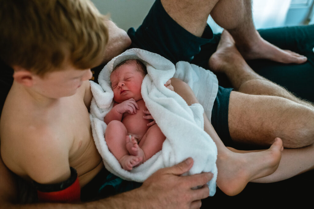 Big brother holding newborn wrapped in towel during first sibling snuggles after home birth