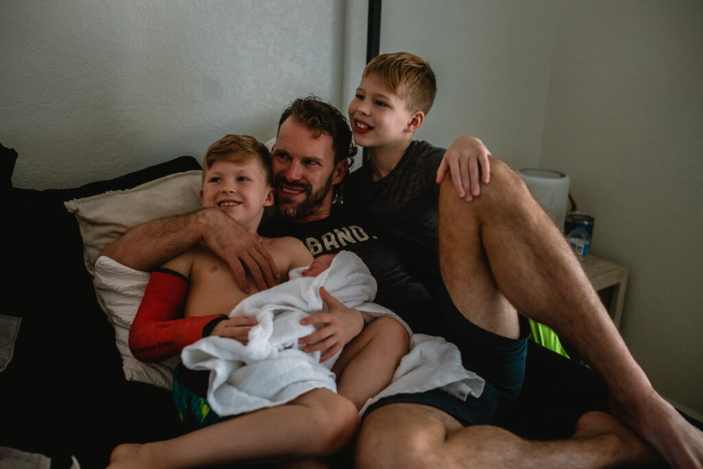Family cuddled together in bed with newborn baby, soaking in quiet bonding moments after birth