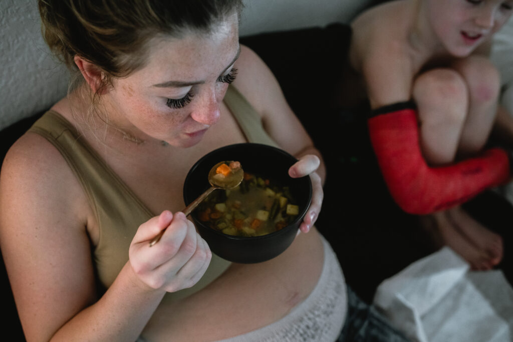 Mother eating warm meal in bed while recovering after home birth, surrounded by family