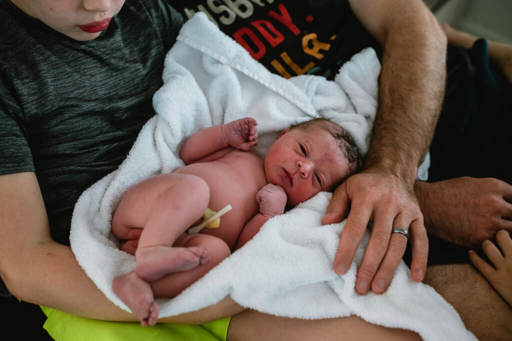 Newborn sleeping peacefully in father’s arms, wrapped in soft blanket after home birth