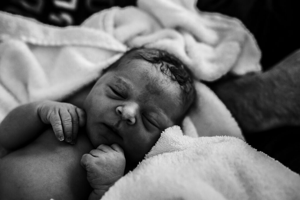 Black and white newborn portrait on blanket, tiny hands curled near face in first hours after birth