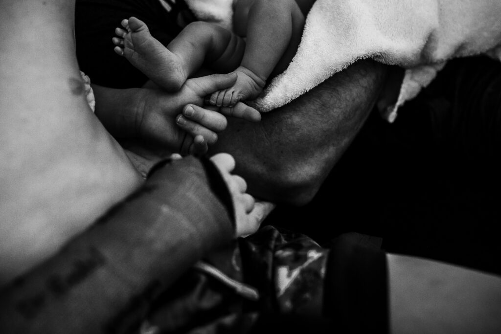 Close-up of newborn feet and siblings’ hands during quiet bonding moments after home birth