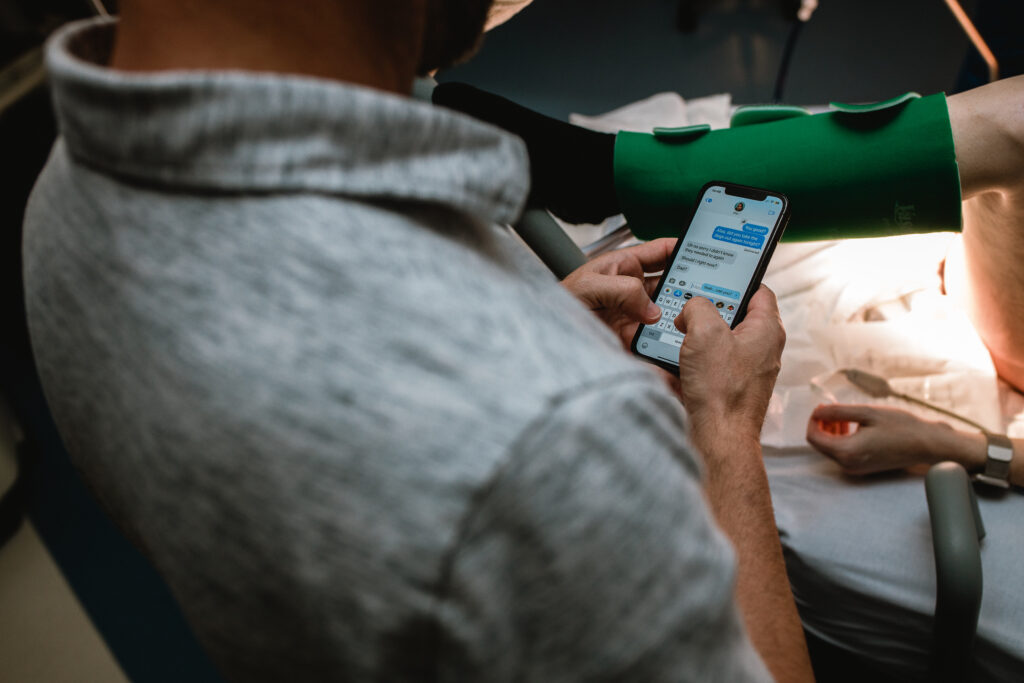 Father checking contraction timing on his phone while supporting his wife during labor