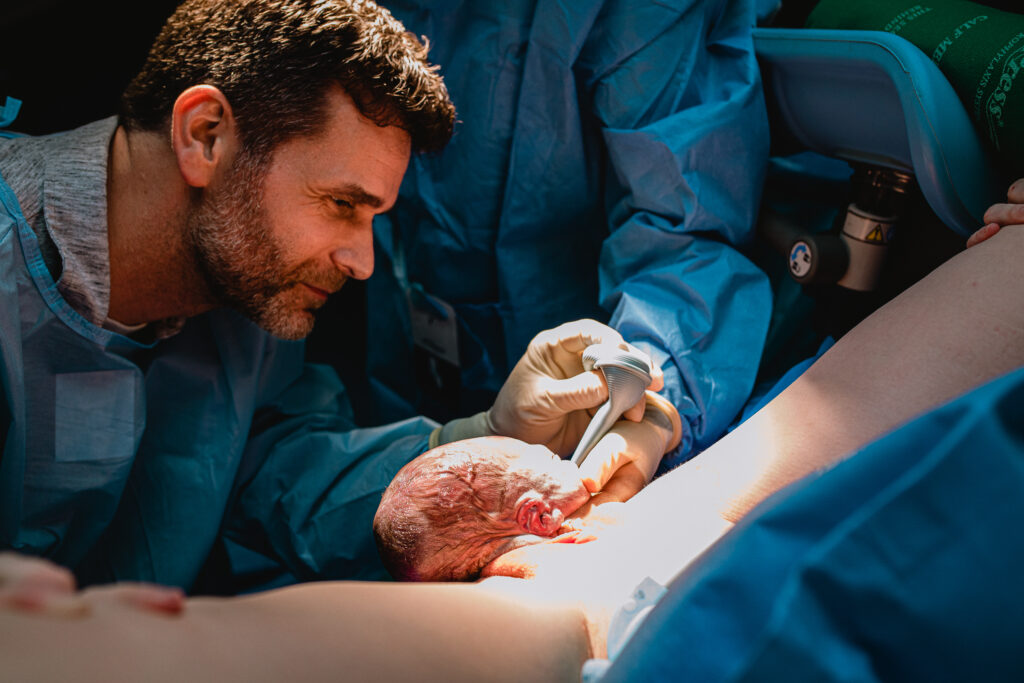 Father catching his newborn baby with guidance from the OB during hospital delivery