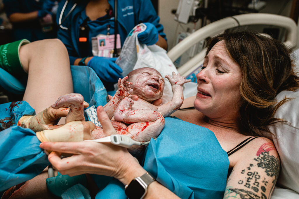 Mother cradling her newborn baby while father sits beside her in quiet relief after birth