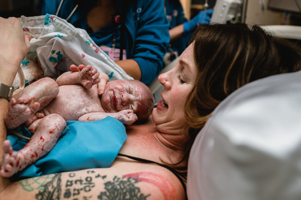 Mother admiring her newborn baby in her arms while father smiles beside her in the delivery room