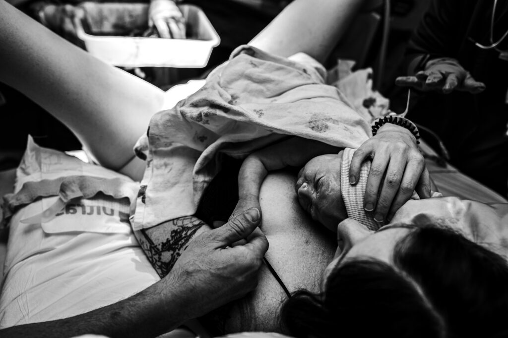 Newborn baby wearing a tiny striped hospital hat while resting peacefully on mother’s chest after delivery