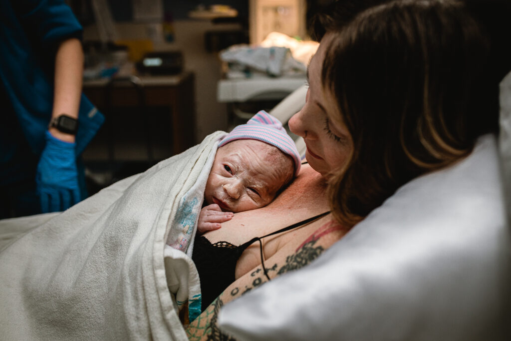 Mother smiling softly while holding newborn swaddled against her chest after a successful hospital birth