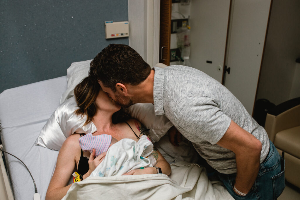 First-time parents smiling at one another while admiring their newborn baby after labor and delivery