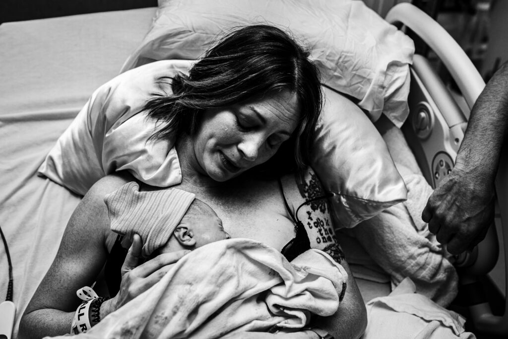 Father leaning down to kiss mother as she holds their newborn baby after an emotional and supportive hospital birth