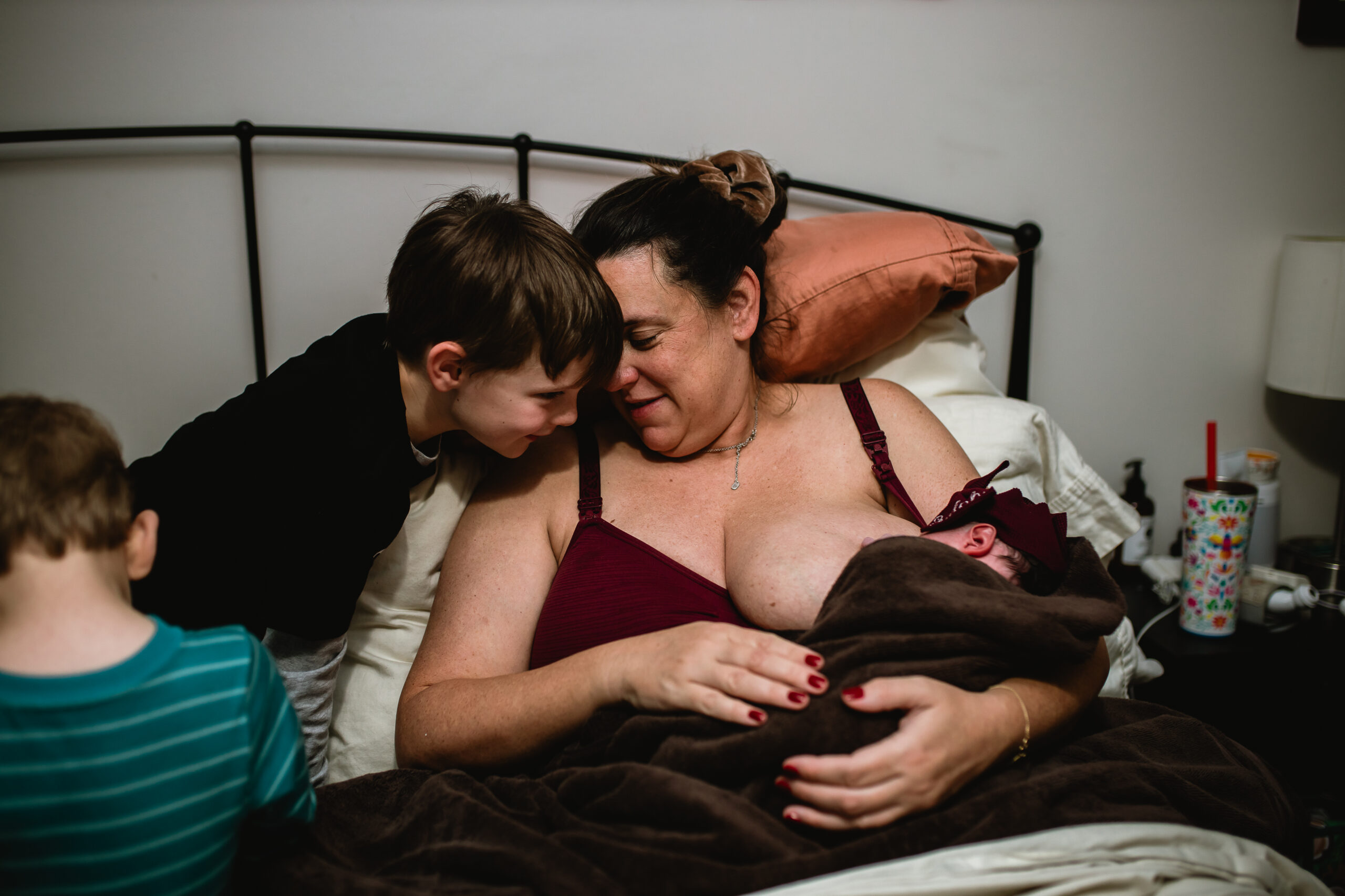 Second-time mother holding her newborn while an older sibling is nearby, captured in a Fort Worth birth photography storytelling style.